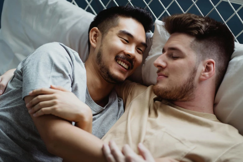 two men cuddled up in bed, one smiling