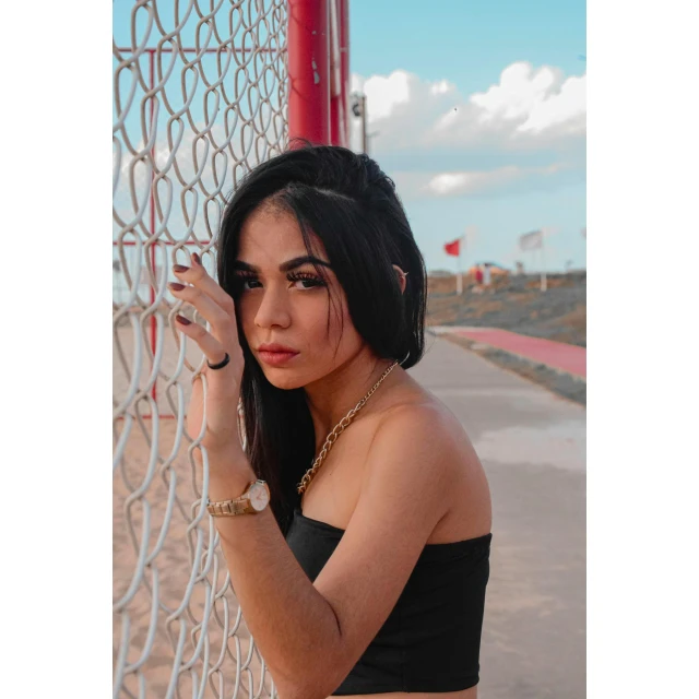 the woman is posing against the fence holding on to it's chain link