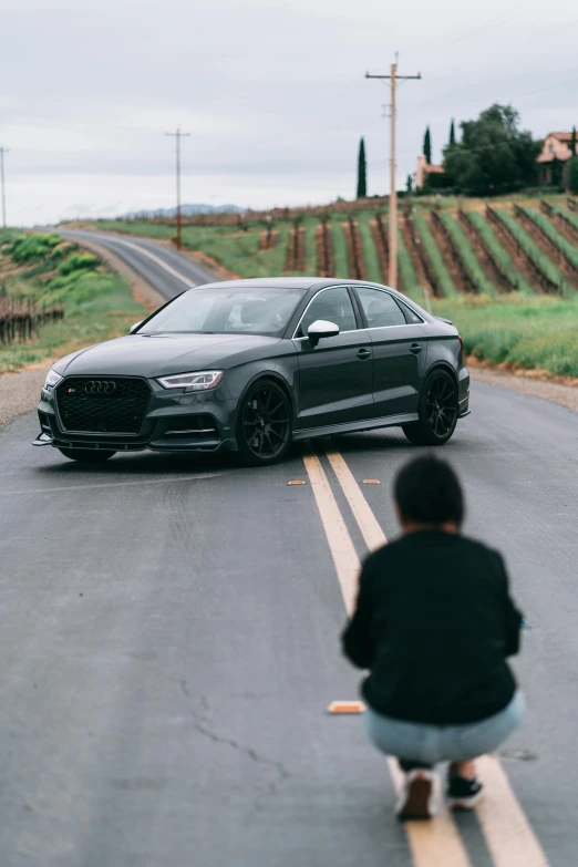 a person sitting on the side of a street in front of a car