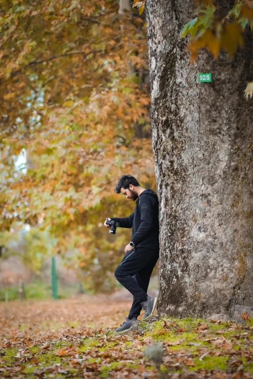 a young man standing next to a tree and holding onto a camera