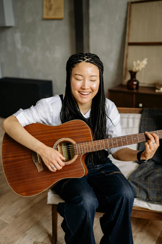 smiling girl with dreadlocks sitting on a chair playing a guitar