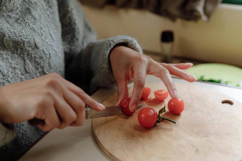 a person with two hands chopping tomatoes on a  board