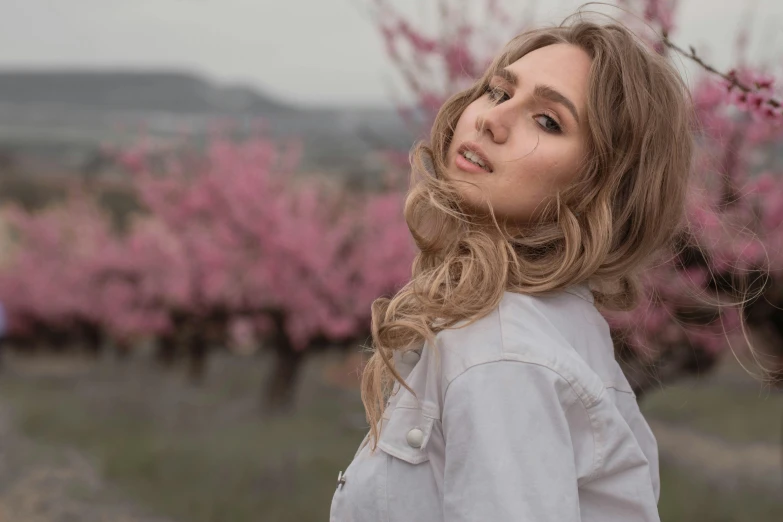 a woman with long, wavy hair stands in front of pink flowers