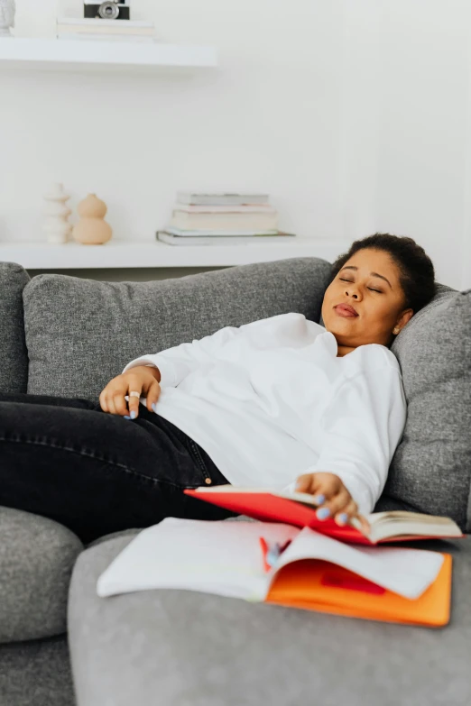 a woman reclines on a couch with books next to her