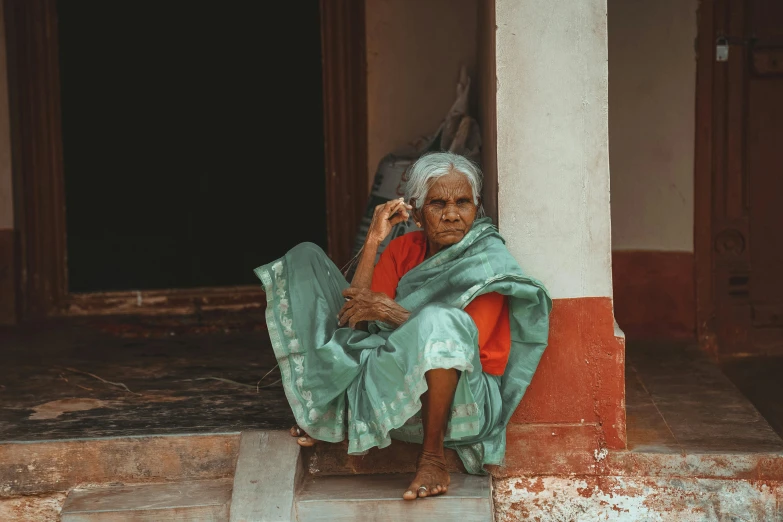 an old woman in green clothes sitting on the corner