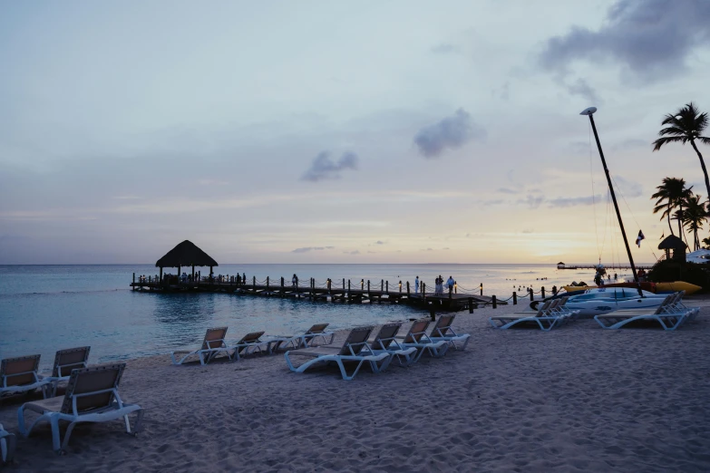 a beach area with lounge chairs and an old pier at sunset