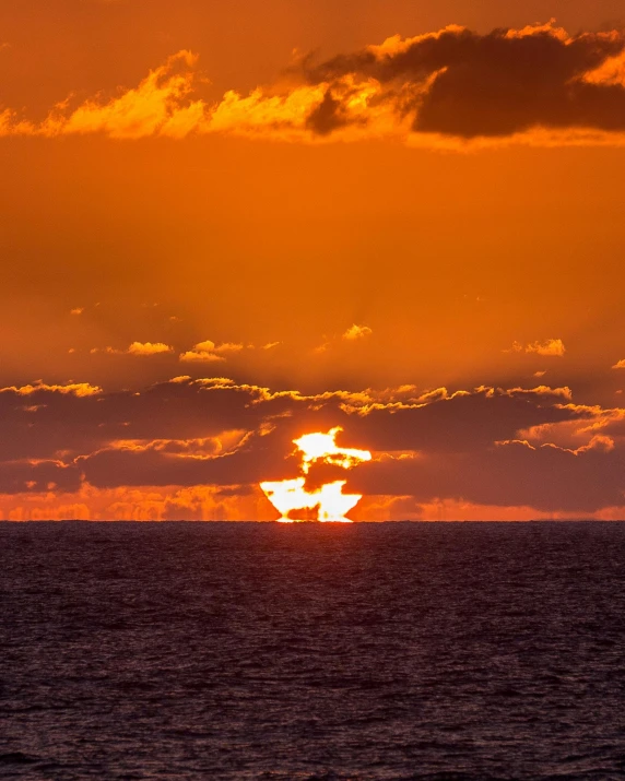 the sun is setting over the ocean on a cloudy day