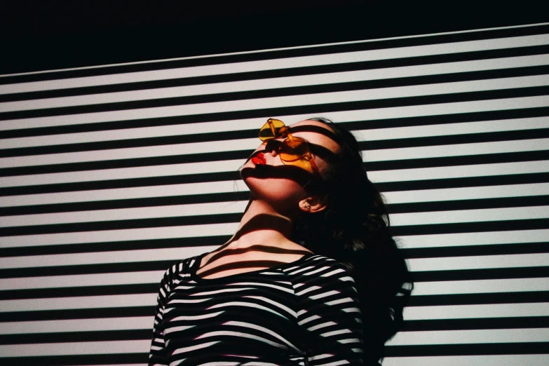 a girl in striped shirt standing against the wall with her eyes closed and flower in her hands