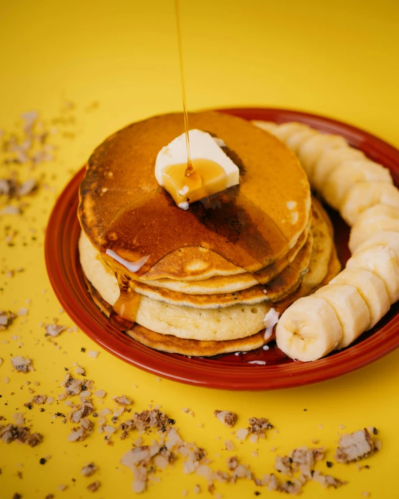 a red plate with a stack of pancakes and banana slices