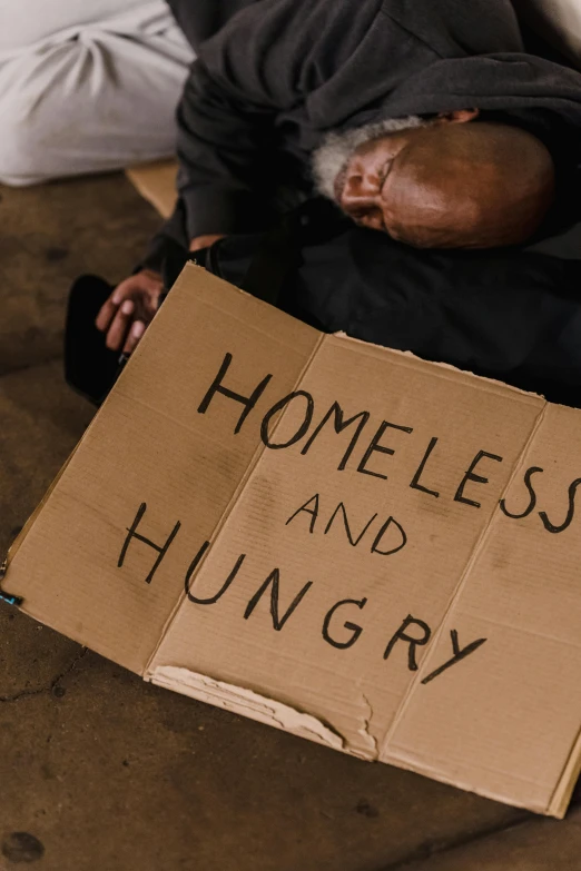 a homeless man sleeps under a cardboard sign