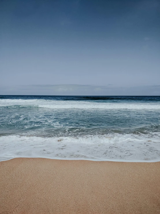 an ocean beach with small waves and a blue sky