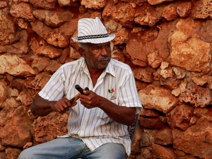 a man sitting down wearing a white hat while holding a cellphone