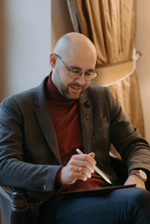 man wearing brown sweater sitting in chair looking down at paper