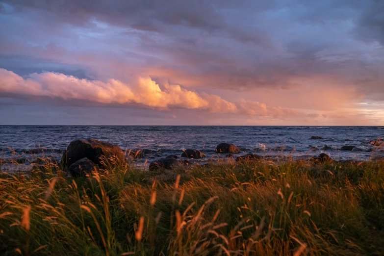 the clouds are over the water and rocks near a beach