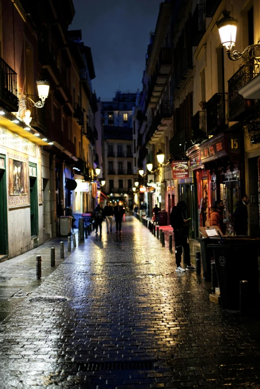 a city sidewalk at night with lights and people on it