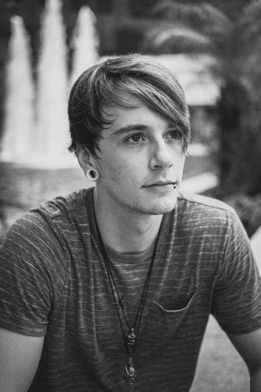 young man sitting on street with fountain in background