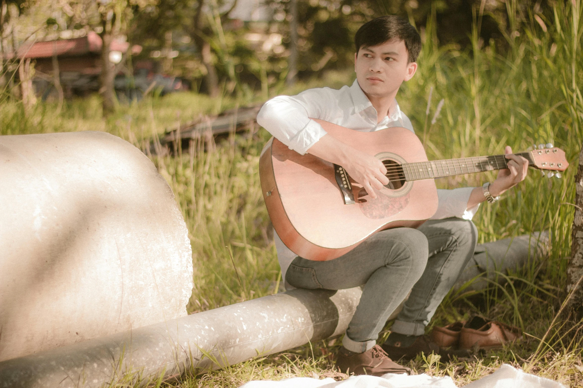 a young man is sitting on a log and playing the guitar