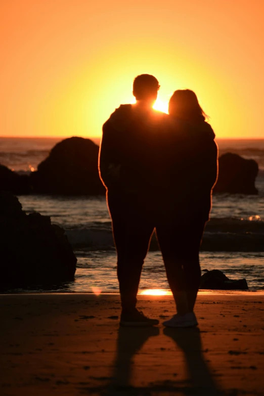 silhouette of two people hugging while the sun sets over the water
