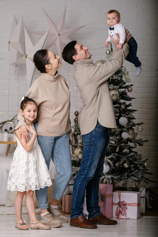 a young family stands next to a christmas tree