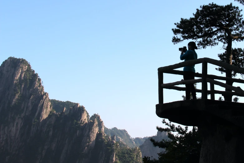 two people are standing on a wooden railing by some mountain