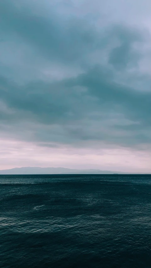 an ocean under cloudy skies with only two people on the beach