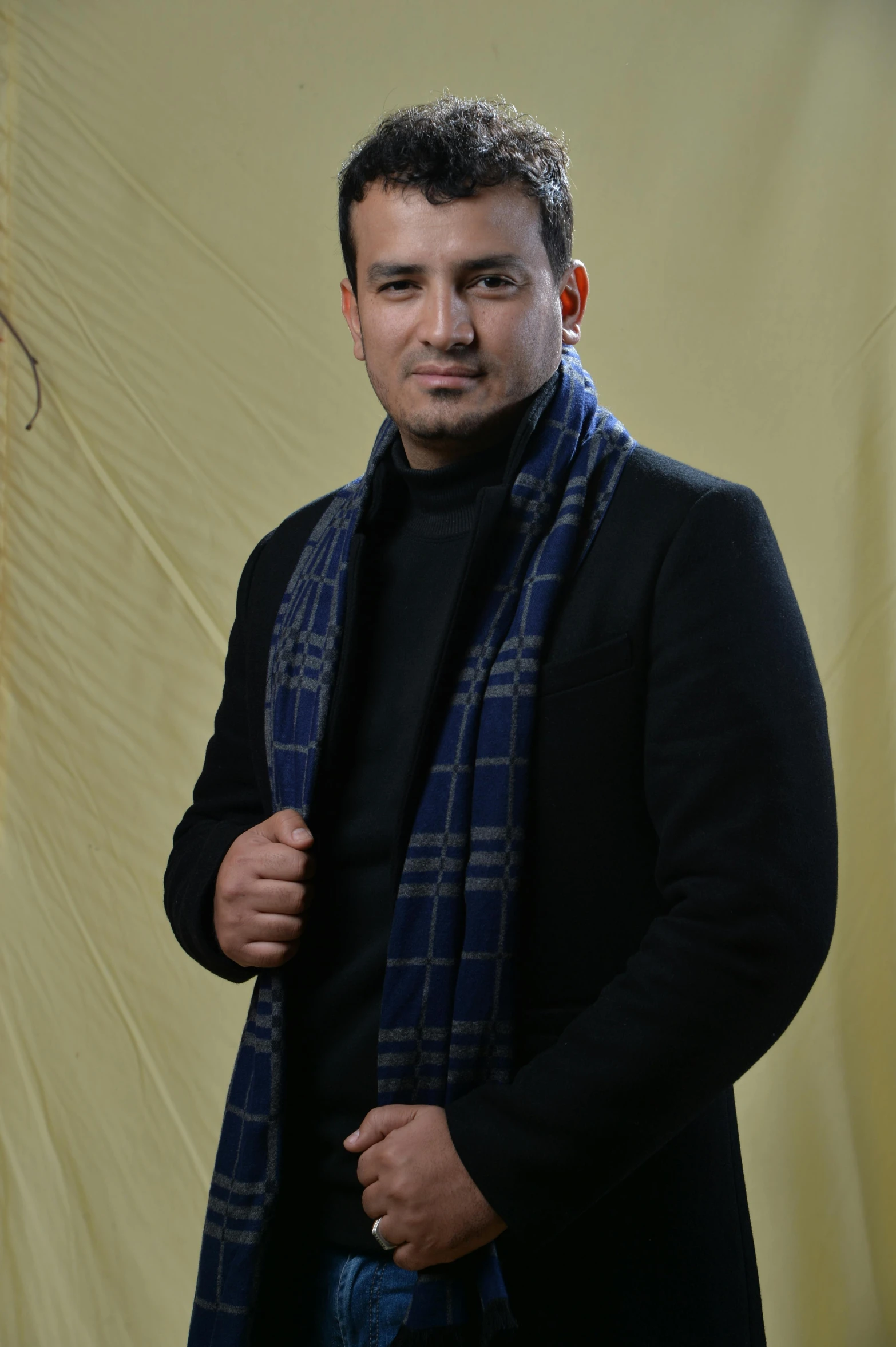 a man in a black sweater standing by a yellow wall