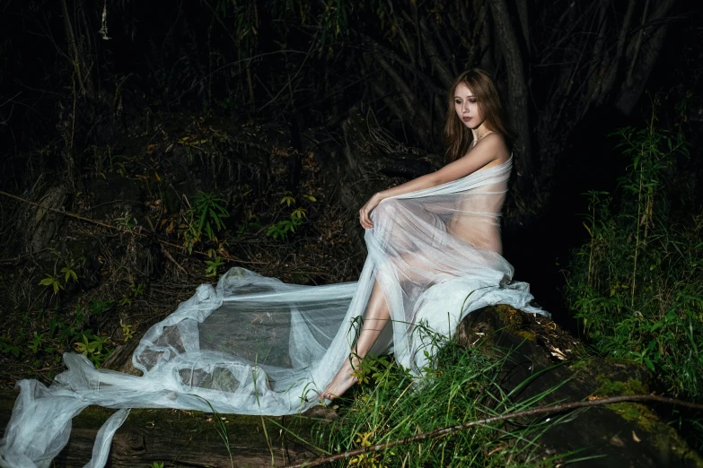 a young woman wearing a dress sitting on a rock in a dark forest