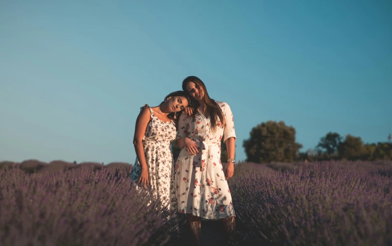 three women wearing dresses stand in the middle of a field