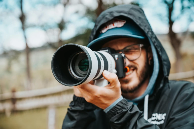 a man with glasses and a hood on taking a picture with a lens