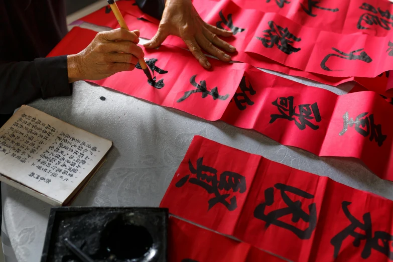 a man writing on some red paper with ink