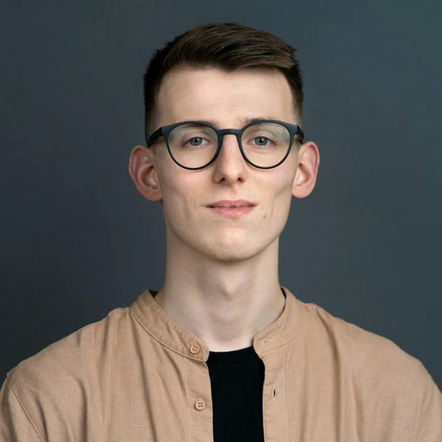 a man wearing glasses standing in front of a gray background