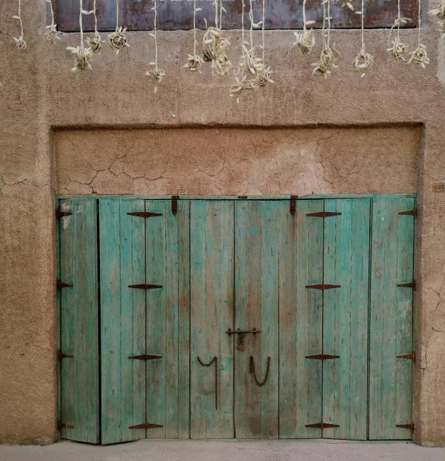 an old brown wall with green doors and two horses drawn on the side