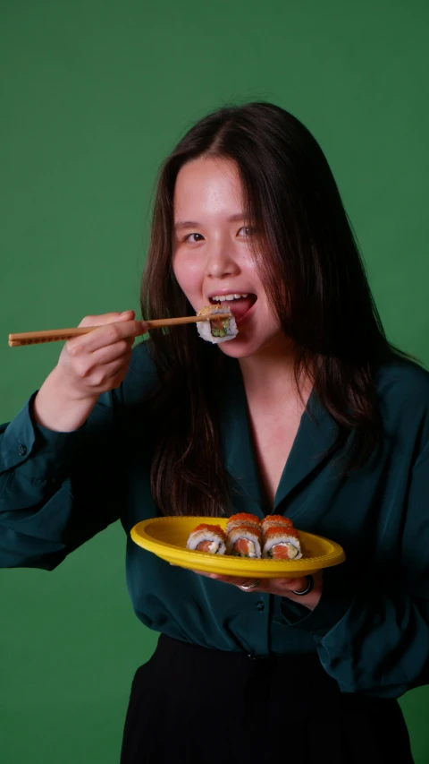 a woman eating sushi from a yellow plate with chop sticks