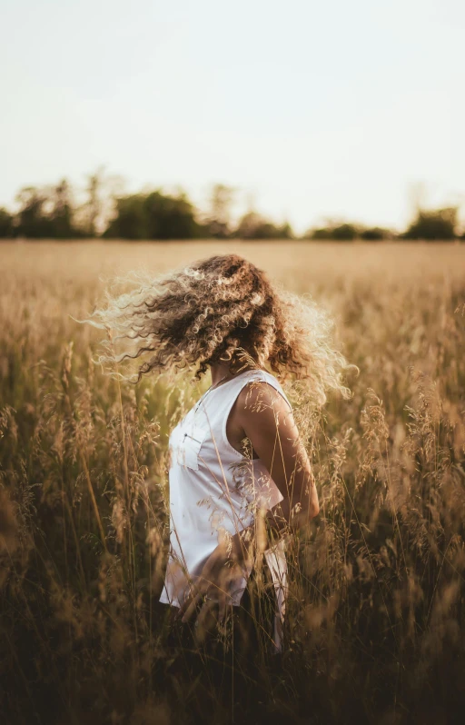 young woman standing in tall grassy field looking back