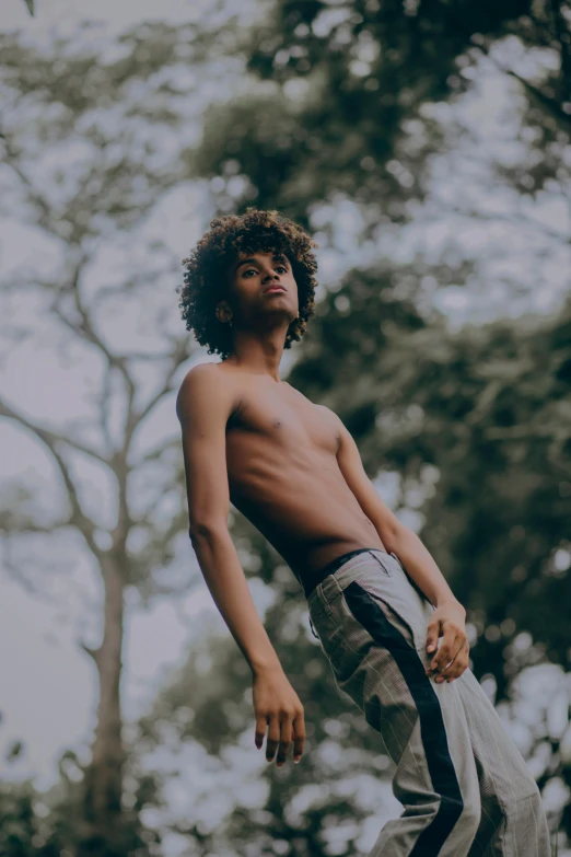 shirtless young man standing next to trees in the sunlight