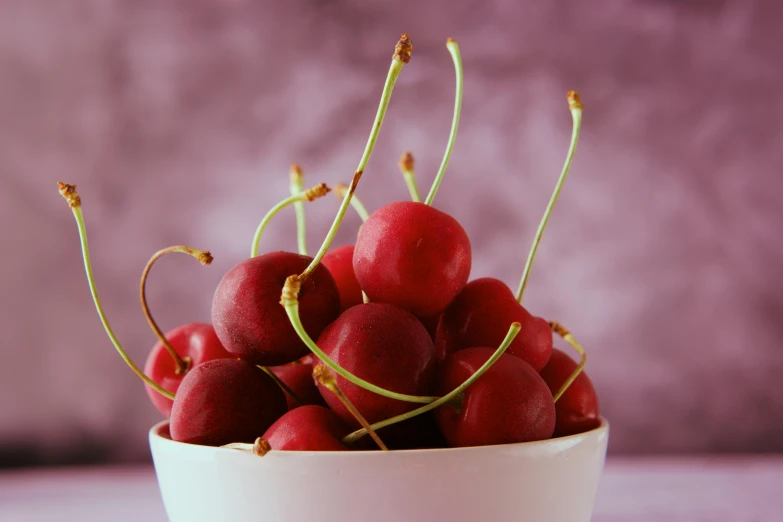 a white bowl filled with red cherries next to a wall