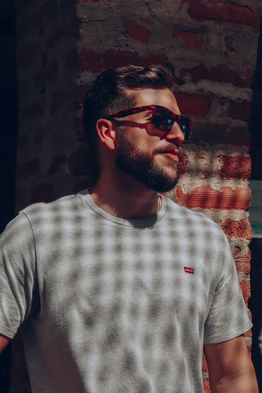 a man standing next to a brick wall with sunglasses on