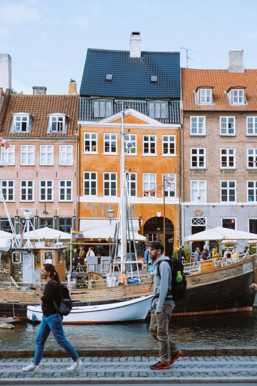 people walking by a river and boats in front of some buildings