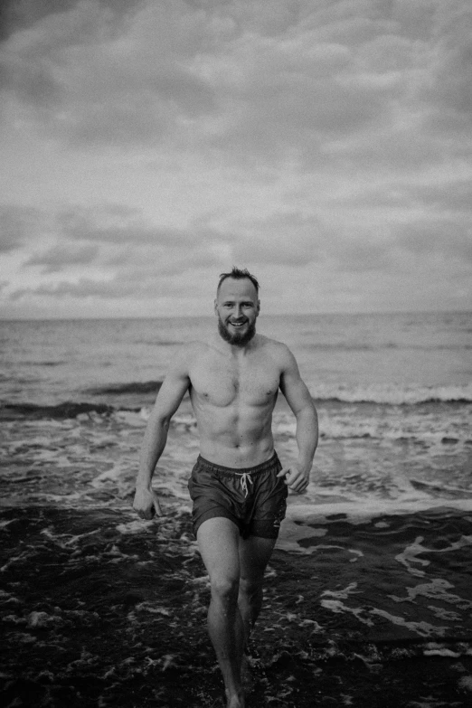 a shirtless man is running on the shore with a surfboard