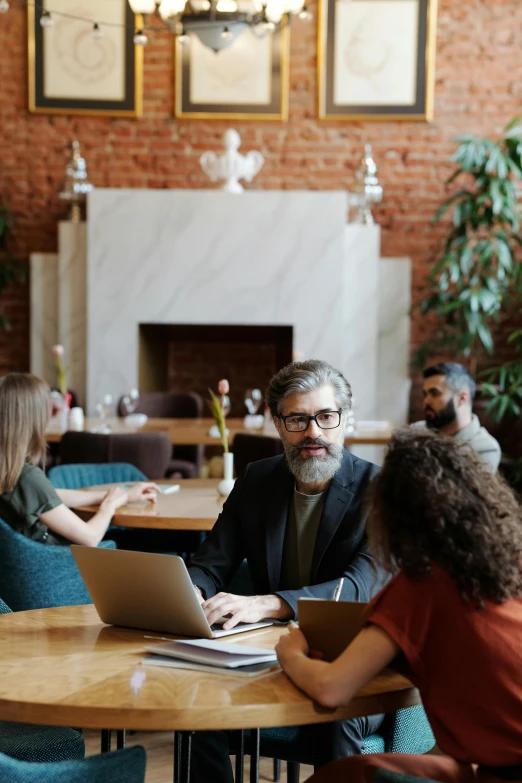 the man sits in a restaurant with two woman on his laptop