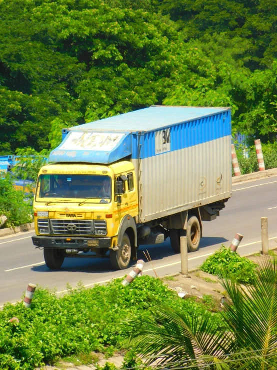 a yellow truck drives down the road in front of a green forest