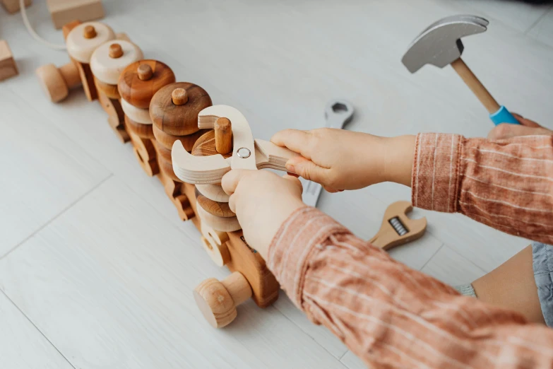 a young person holding a toy wrench on a long row of wood toys