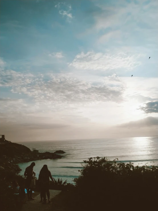 two people walking towards the beach with the sun in the background