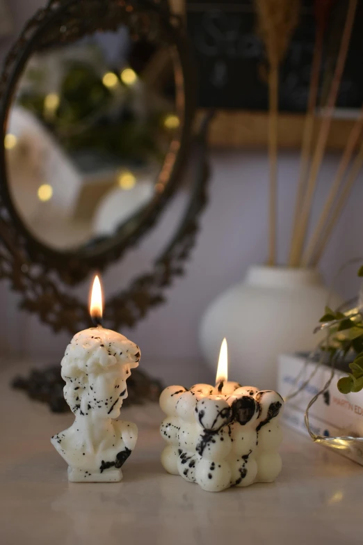 two candles on a table with an object in the background