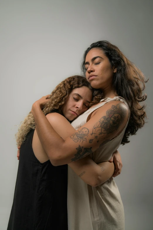 two women hug in front of a white wall
