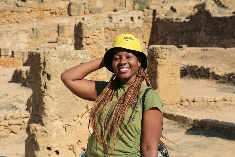 a woman wearing a yellow construction hat smiles in front of ruins