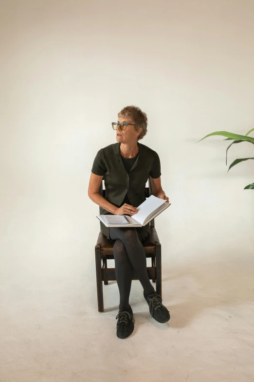 a man with short hair and glasses sits on a chair reading a book