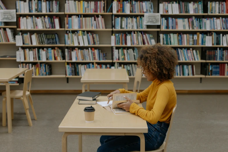 young woman sitting at a table in front of a bookshelf reading