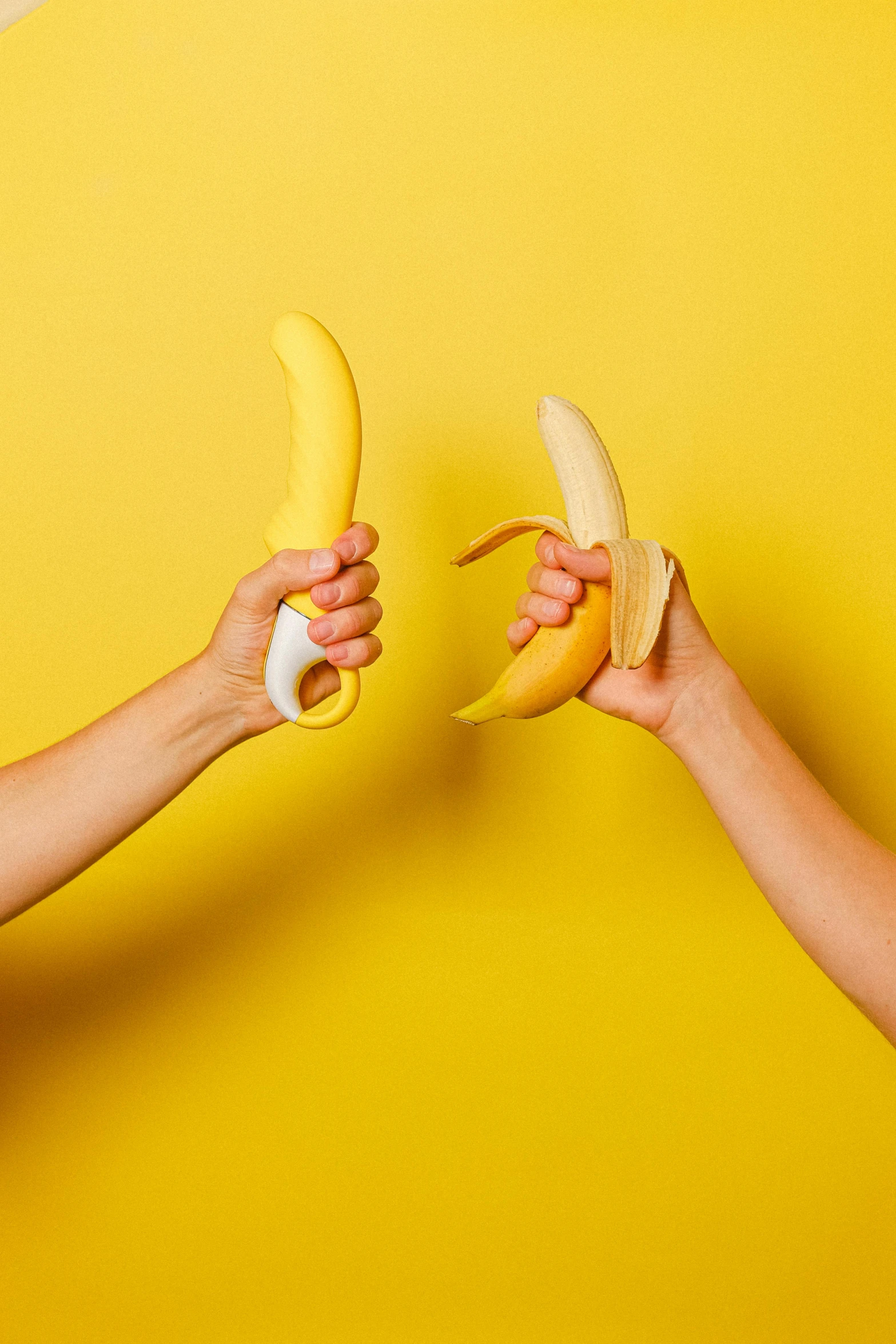 two hands holding two bananas against a yellow background