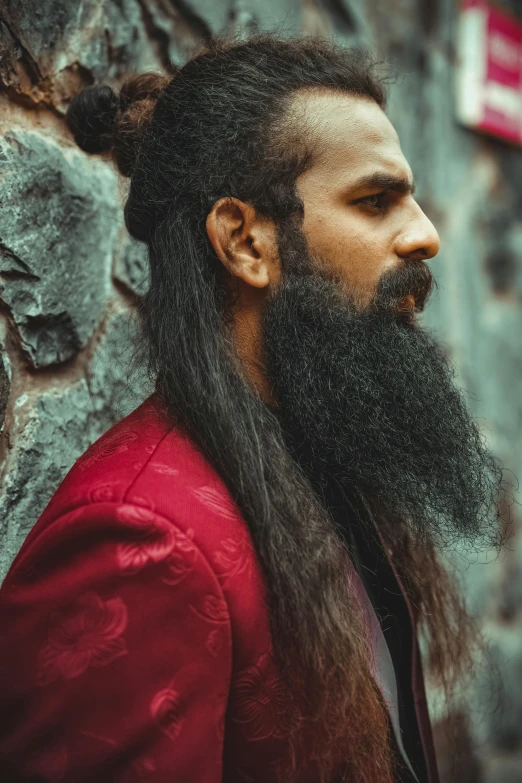 a man with long black hair and a beard wearing a red jacket